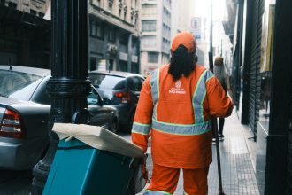 Trabalhador da limpeza urbana carrega equipamentos em uma rua de São Paulo.
