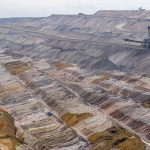 Vista aérea de uma mina a céu aberto, com máquinas de mineração e camadas de solo expostas.