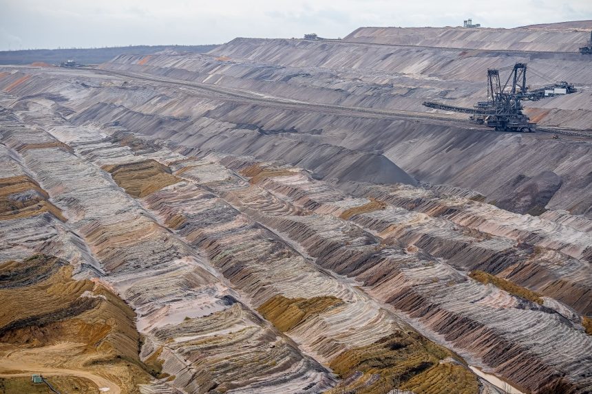 Vista aérea de uma mina a céu aberto, com máquinas de mineração e camadas de solo expostas.