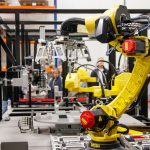 Braço robótico amarelo operando em uma instalação industrial moderna.